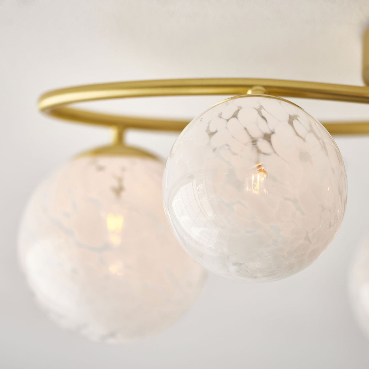 Close-up of two white speckled glass globes on a gold ceiling light, showing the intricate pattern.
