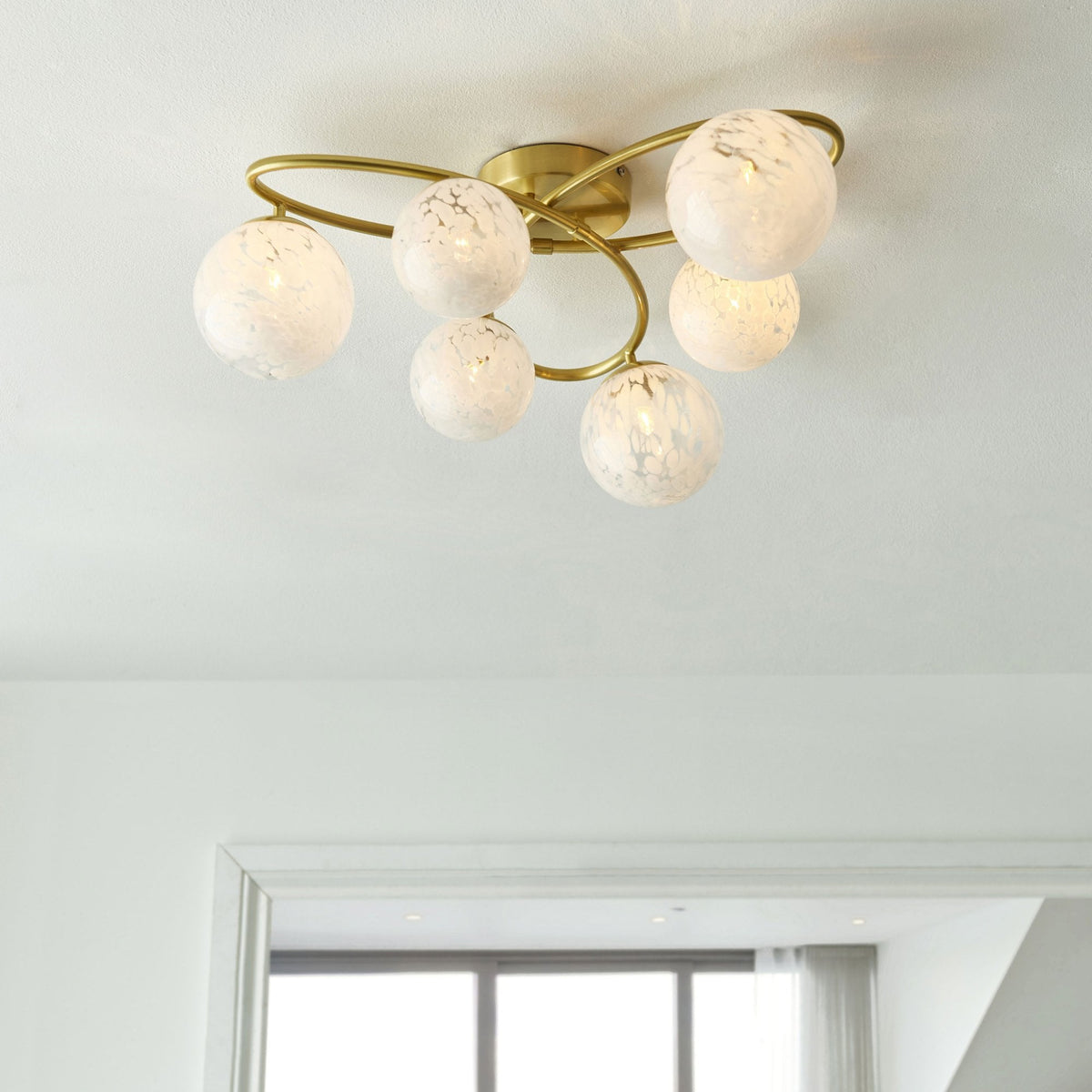 Gold ceiling light with six white speckled glass globes, illuminated, in a modern white room.