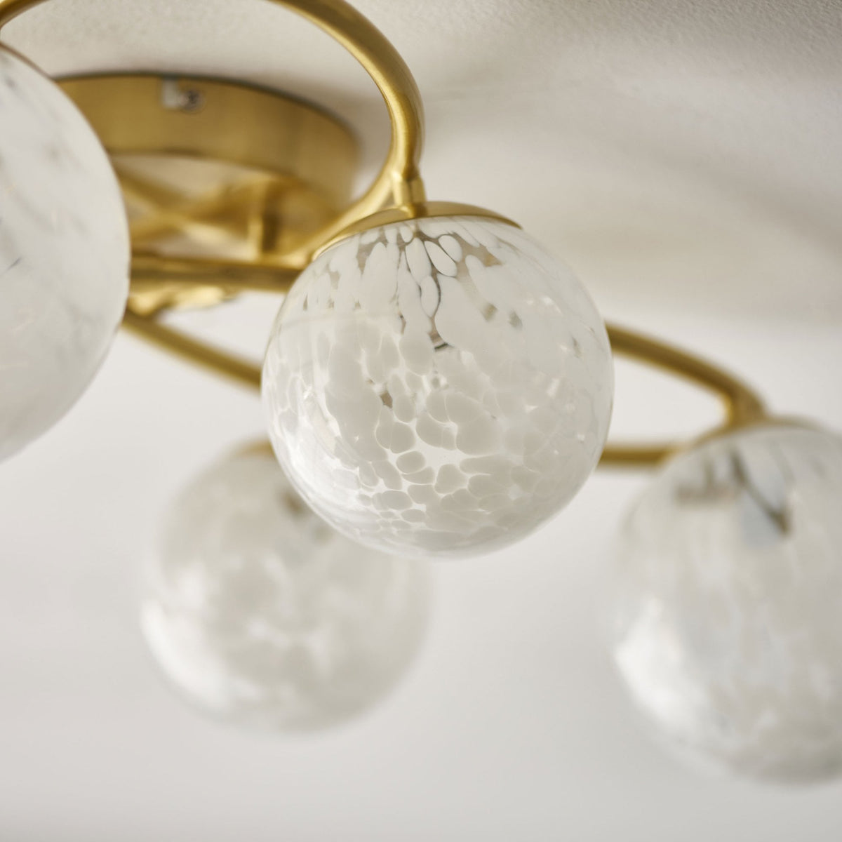 Detailed view of a white speckled glass globe on a gold ceiling light, highlighting its texture.