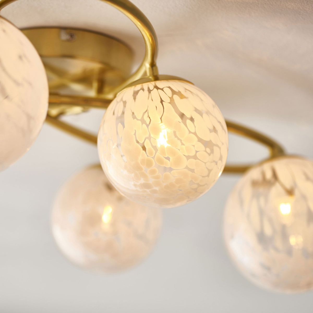 Close-up of an illuminated white speckled glass globe on a gold ceiling light, showing its warm light.