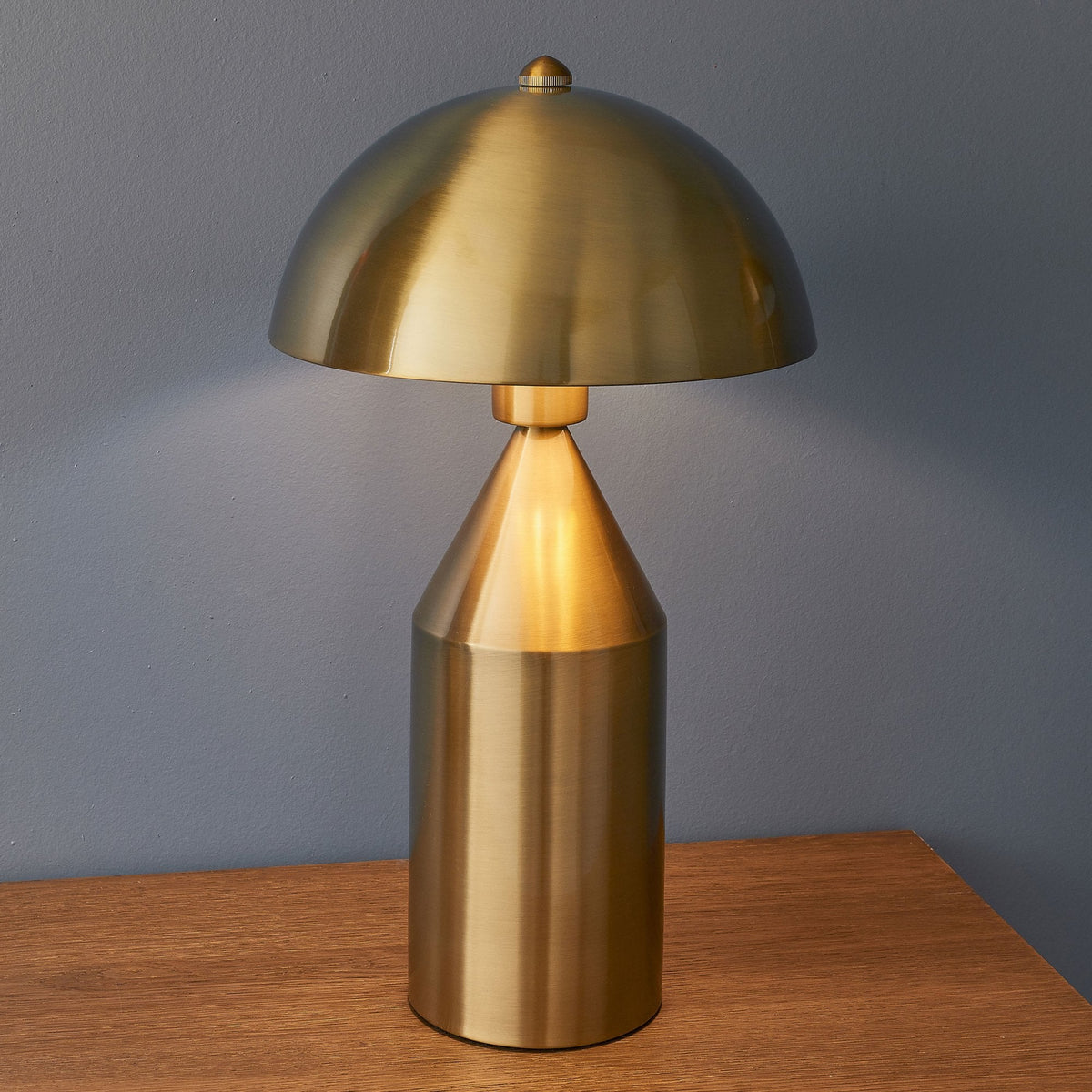 A gold table lamp with a mushroom-shaped shade casts a warm glow on a wooden surface.