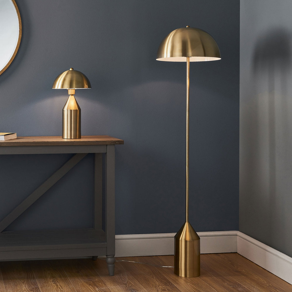 A gold table lamp and a matching floor lamp illuminate a room with a dark blue wall.