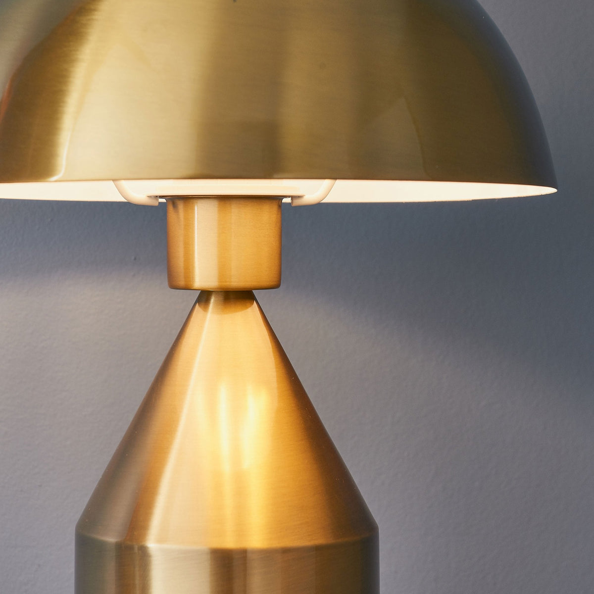 Close-up of the base of the mushroom-shaped shade of a gold table lamp, showing the light source.