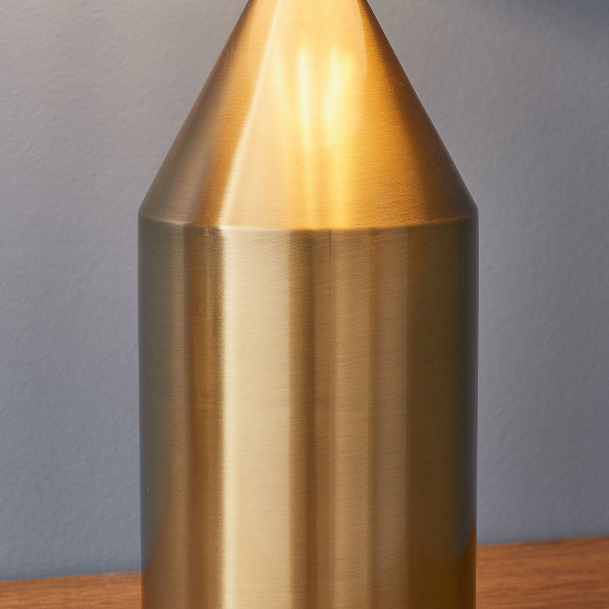 Close-up of the cylindrical base of a gold table lamp, resting on a wooden surface.