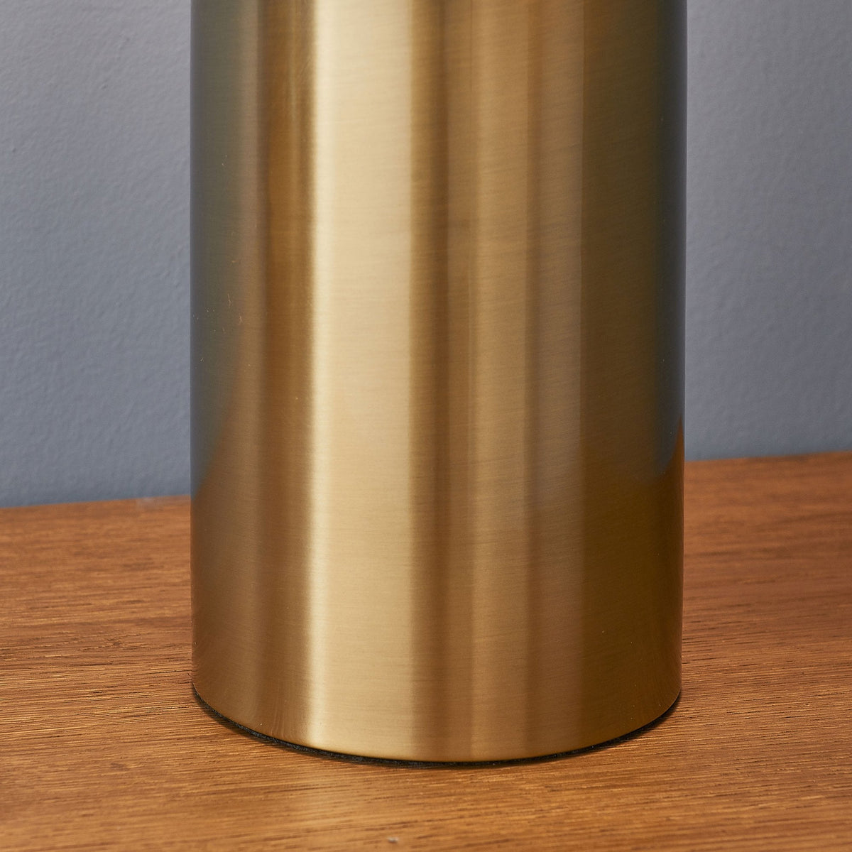 Close-up of the bottom of the cylindrical base of a gold table lamp on a wooden surface.