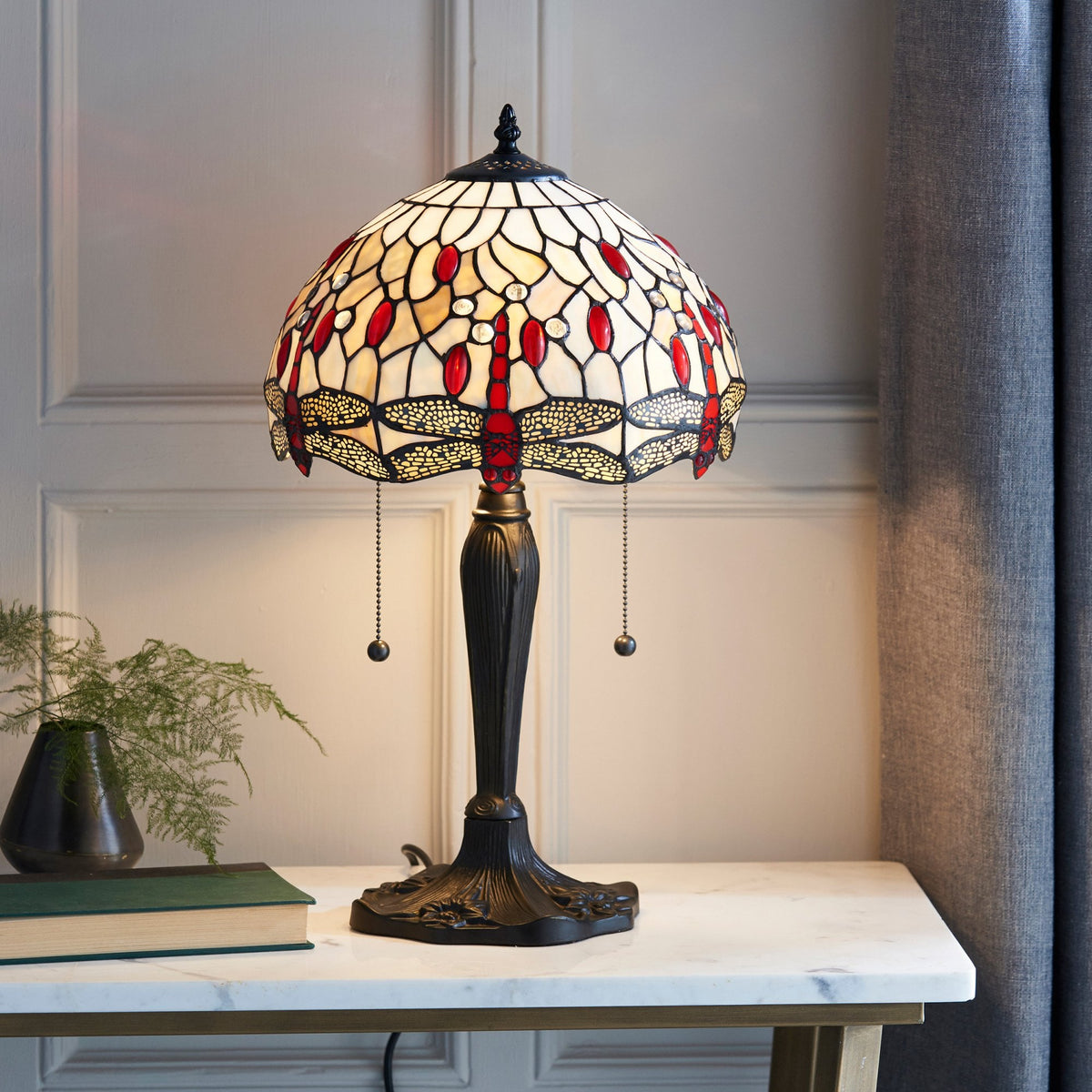 A Tiffany table lamp with a stained glass shade featuring dragonflies, on a white marble table.