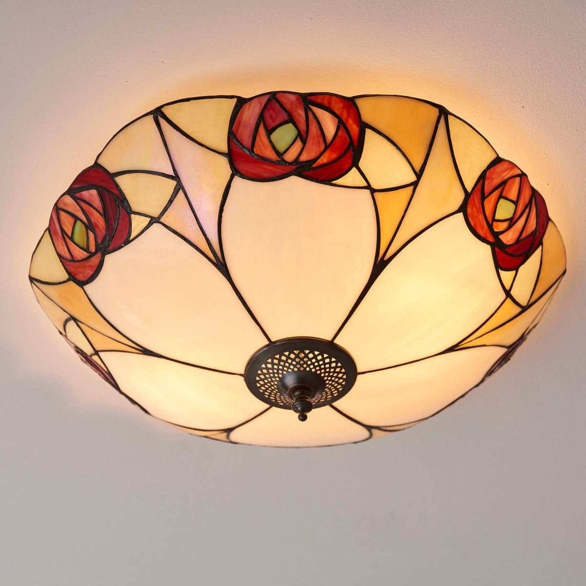 A close-up of a ceiling light featuring a stained-glass rose design, radiating a warm glow.