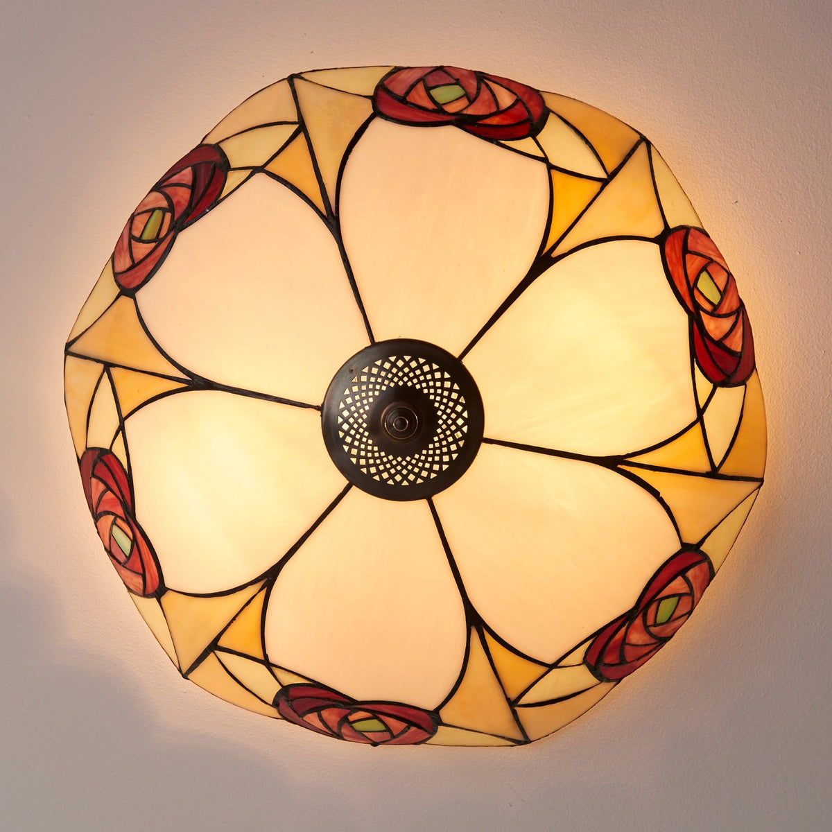 A close-up of a ceiling light featuring a stained-glass rose design, radiating a warm glow.