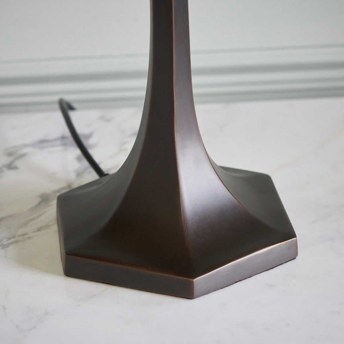 The dark bronze base of a Tiffany lamp on a marble surface.