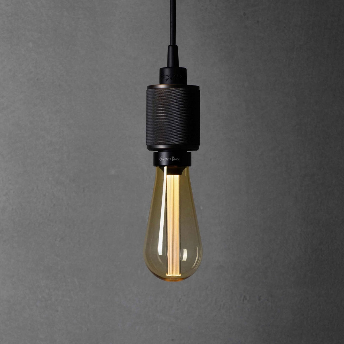 A close-up of a black pendant light with a textured metal casing and a warm, amber-tinted LED bulb.