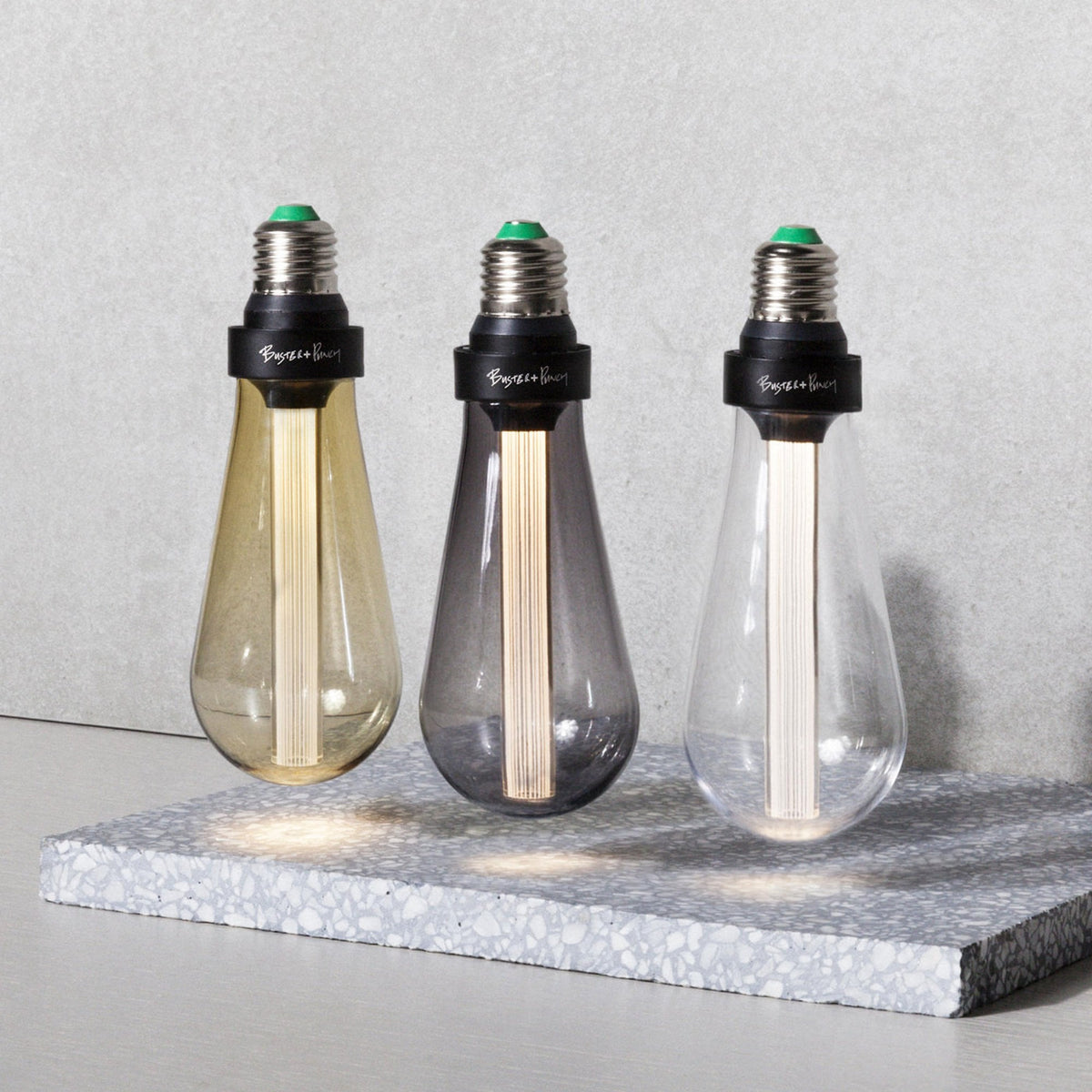 Three Buster + Punch LED light bulbs in amber, smoked, and clear glass on a terrazzo surface.