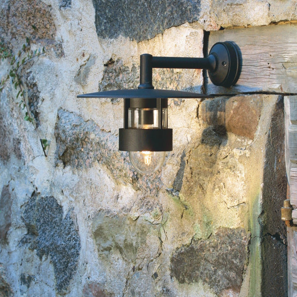 A black outdoor wall light illuminates a textured stone wall, showcasing the fixture's design.