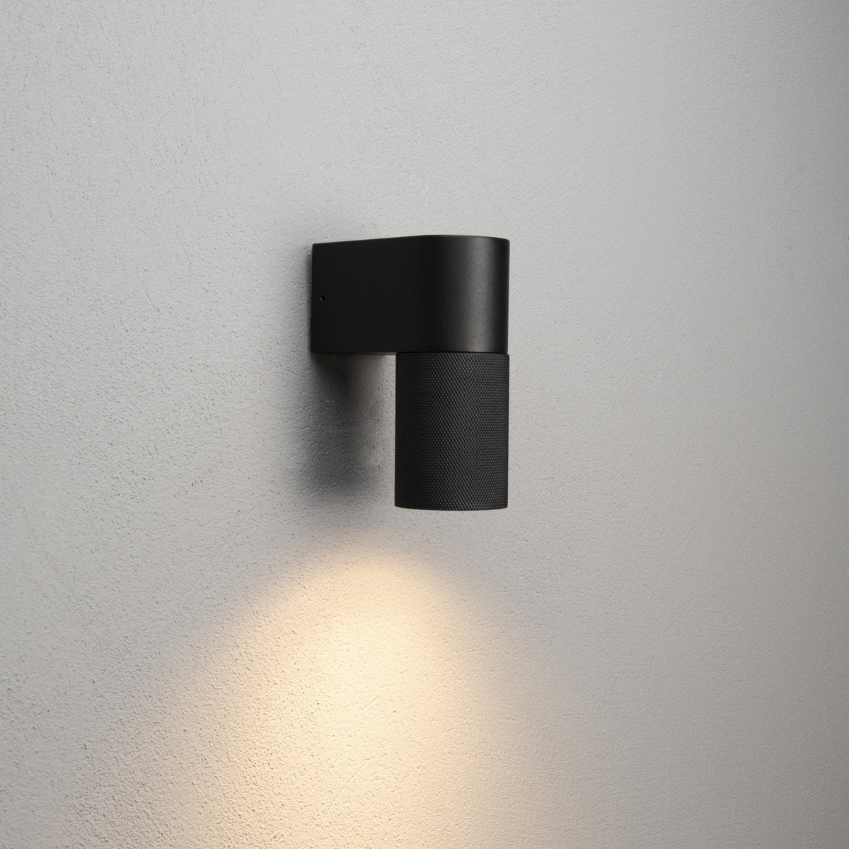 A sleek black wall light illuminating a warm glow downwards onto a light grey wall.