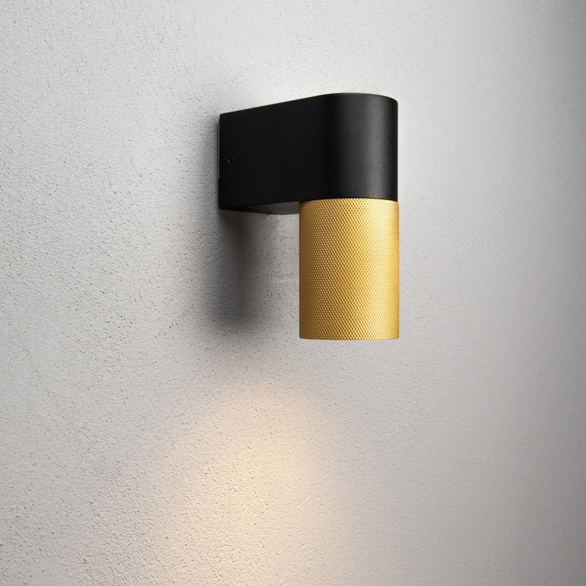 A black and gold wall light illuminating a white wall, showcasing its warm glow.
