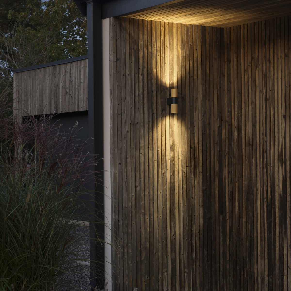 An illuminated outdoor wall light on a wooden wall, casting light upwards and downwards.