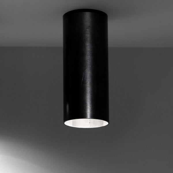 A black cylindrical spotlight casting a bright glow downwards onto a surface.