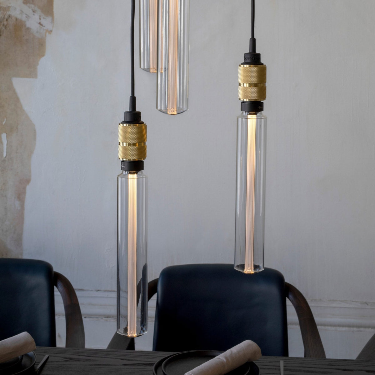 Three pendant lights with clear glass shades and brass fittings hang above a dark dining table.