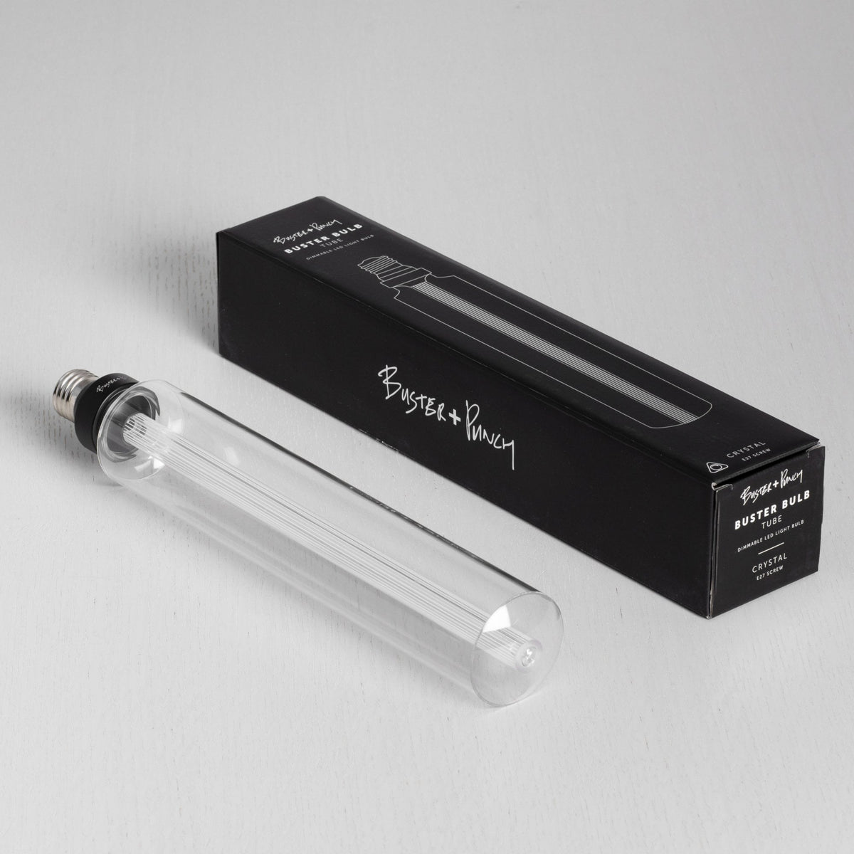 A Buster + Punch Buster Bulb tube light bulb and its black packaging on a white surface.