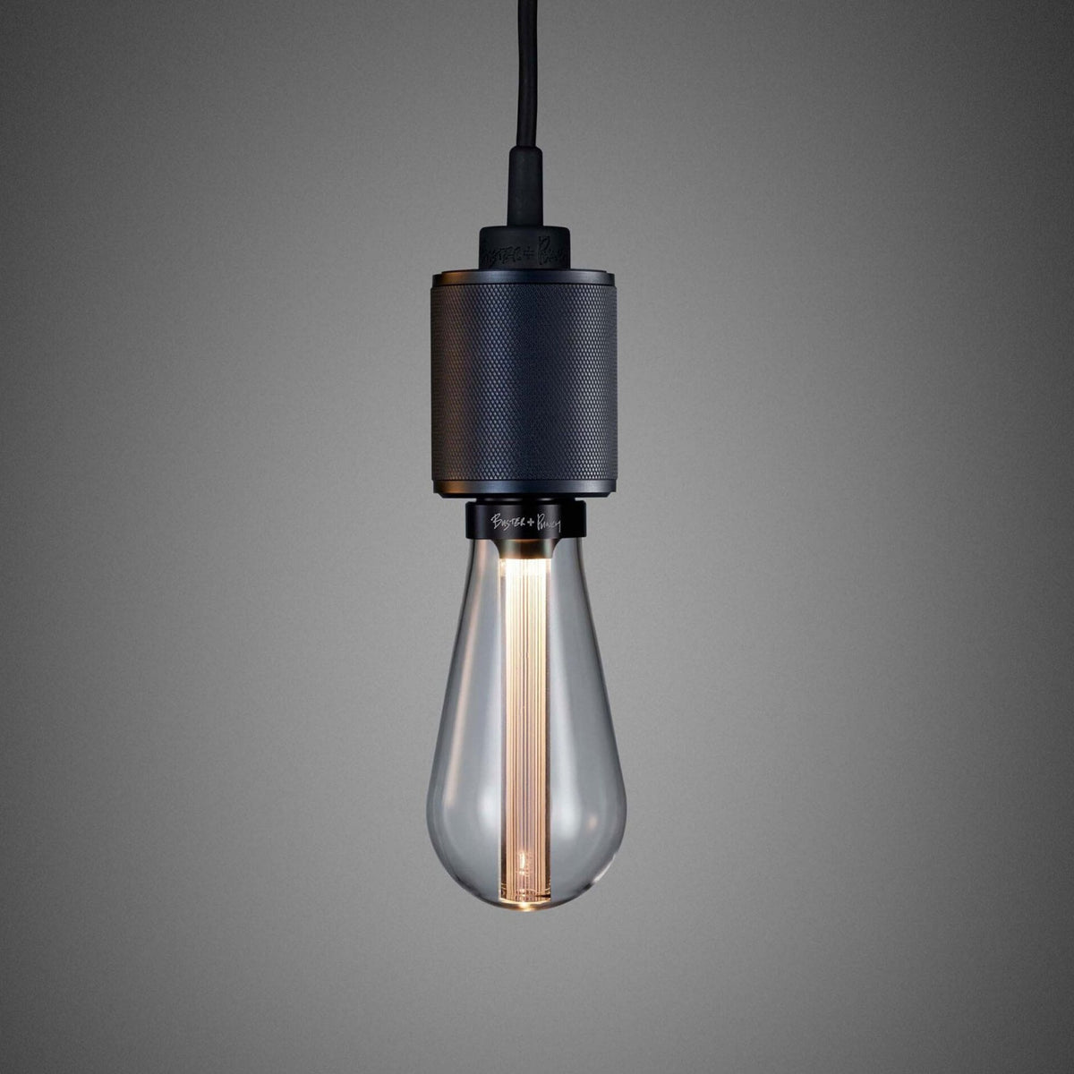 A close-up of a dark grey pendant light with a clear, teardrop-shaped bulb against a grey background.