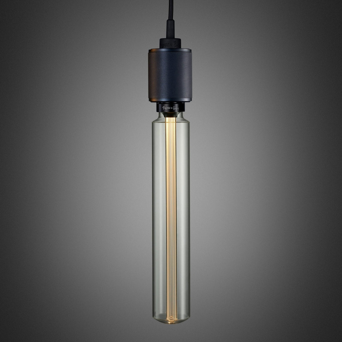 A long, clear glass light bulb with a textured black metal base, hanging against a dark grey background.