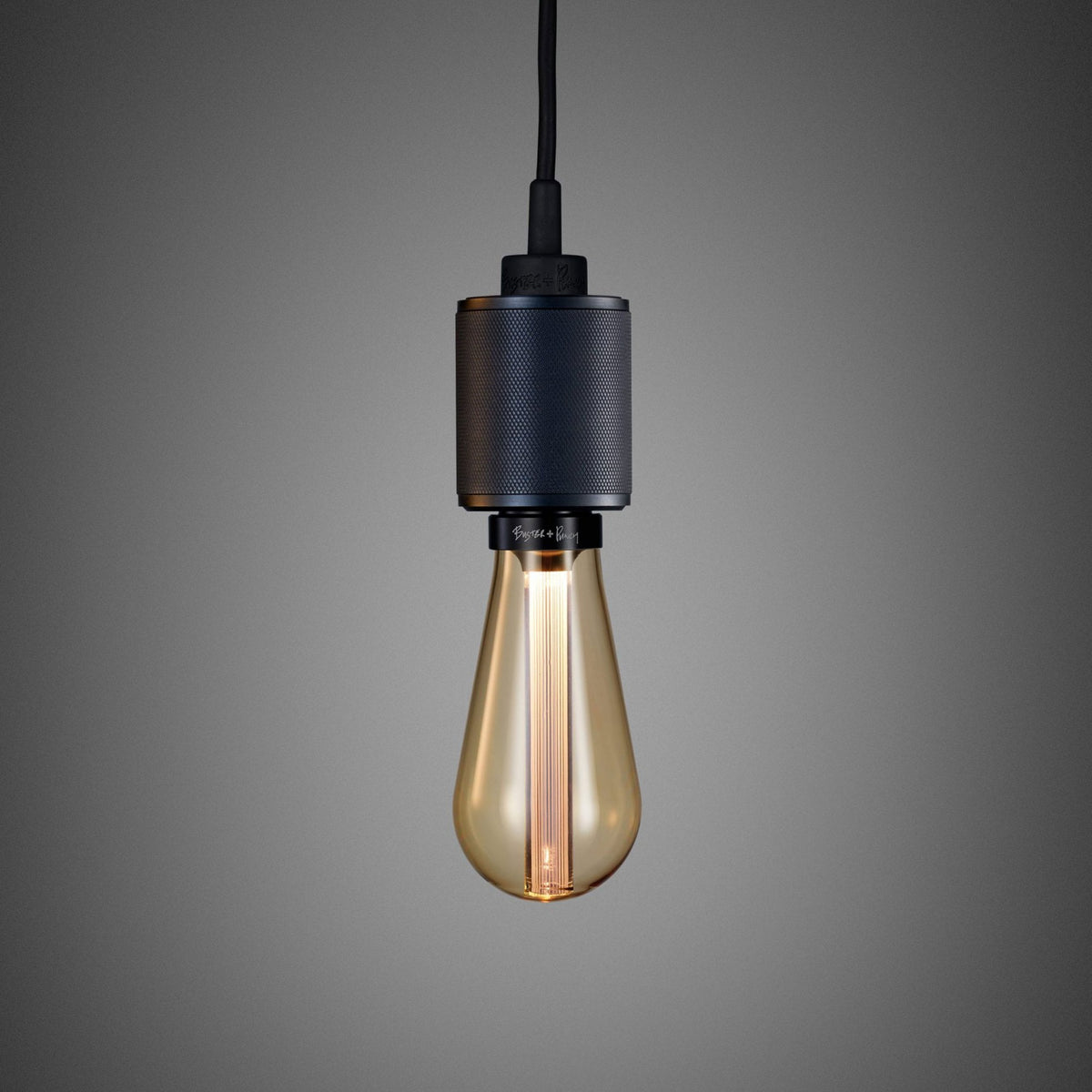 A close-up of a black pendant light with a textured metal casing and a warm, glowing Edison bulb.