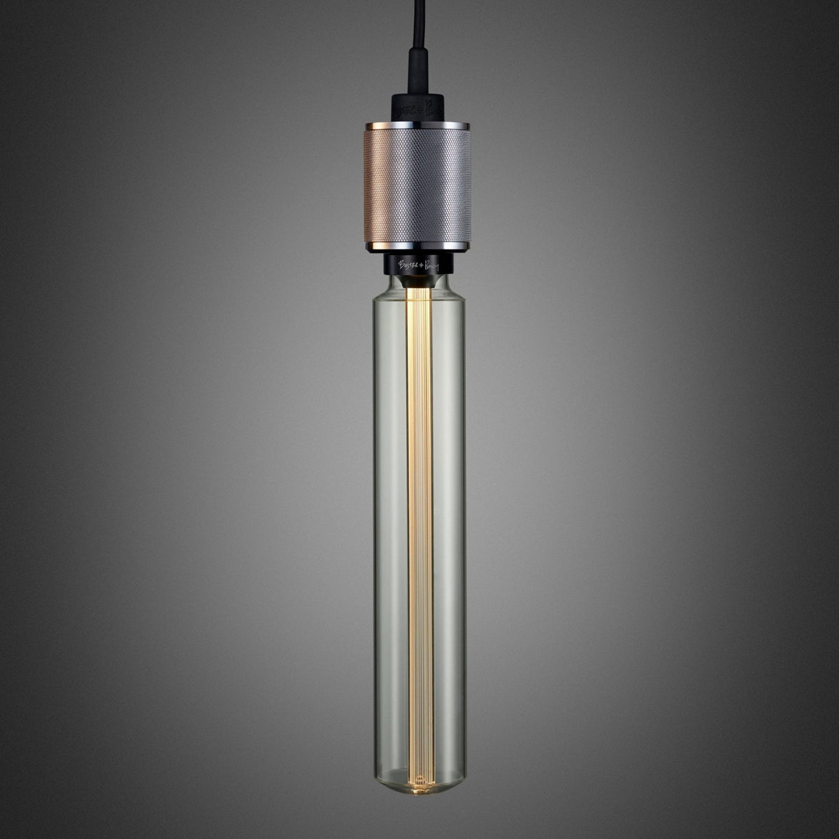 A long, clear glass light bulb with a metallic, textured base, hanging against a dark grey background.
