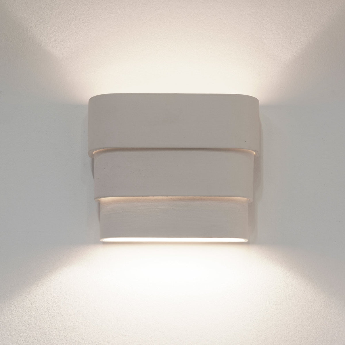 A contemporary, rectangular wall light with three layers, emitting warm light in an upward and downward direction.