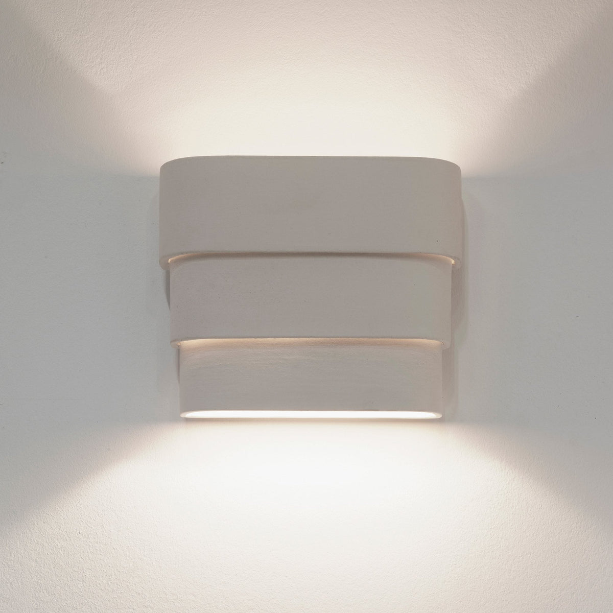 A white, three-tiered rectangular wall light glowing with warm light upwards and downwards.