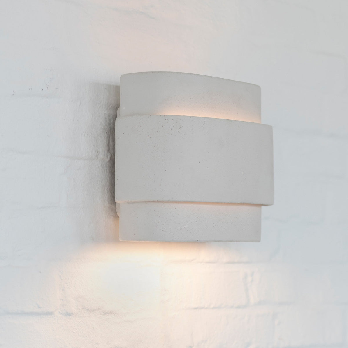 A modern wall sconce casts light upwards and downwards on a white brick wall.