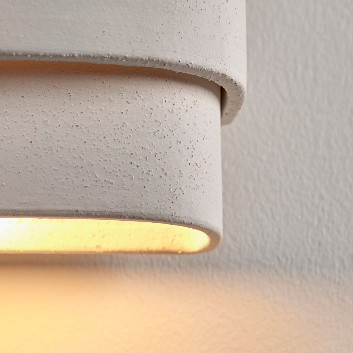 Close-up of a white textured wall light showing warm light emanating from below.