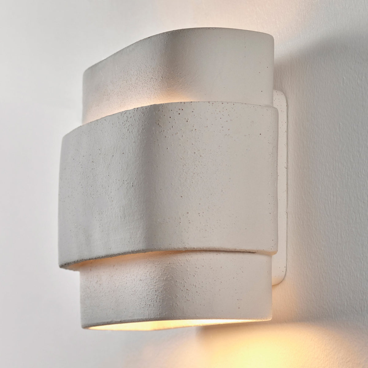 A textured white modern wall light illuminates a white wall upwards and downwards.