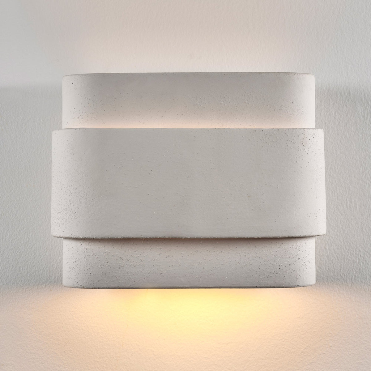 A square white modern wall light with a textured surface, illuminating a white wall.