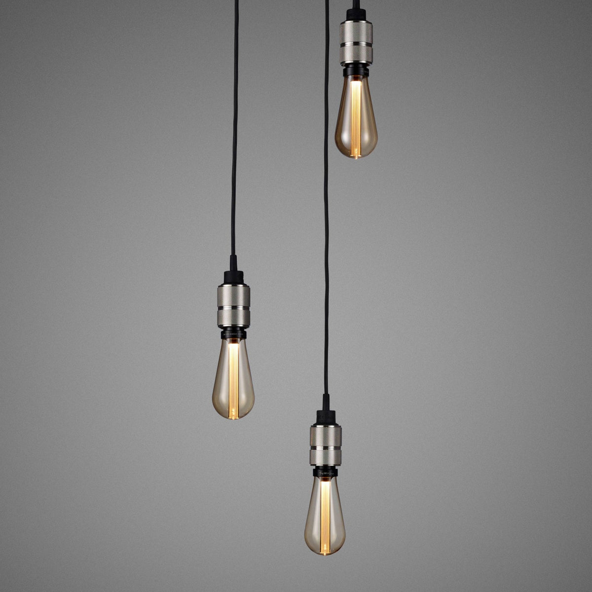 Three pendant lights with exposed filament bulbs hang against a gray background.