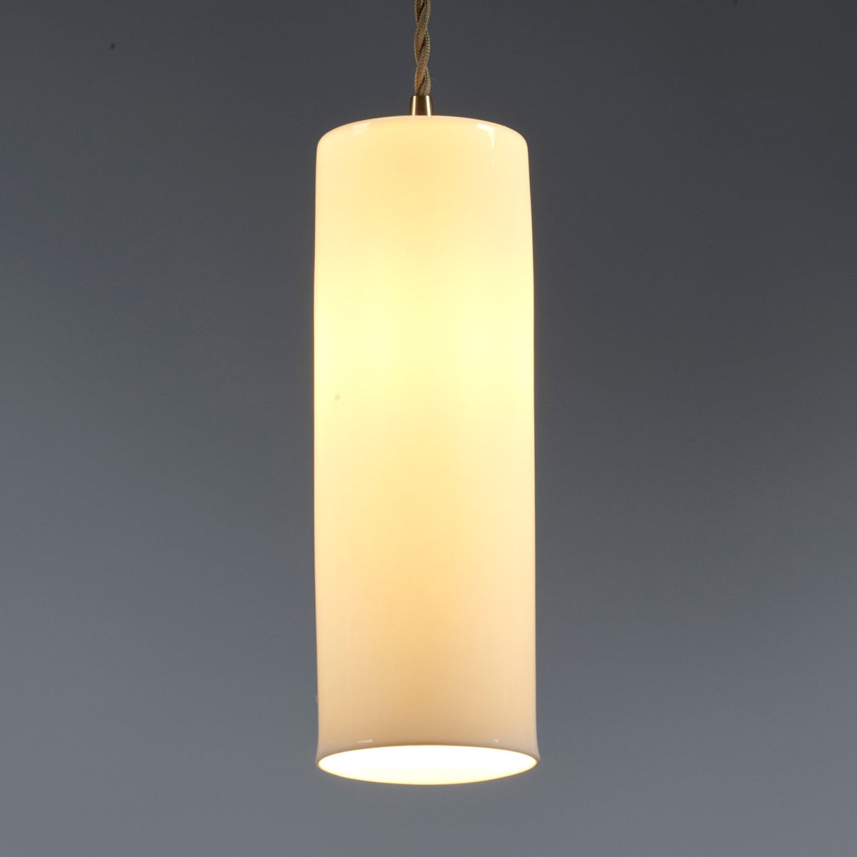 The illuminated white cylindrical pendant light, emitting a warm and inviting glow.