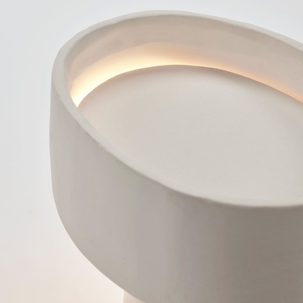 Close-up of the lit oval top of a white ceramic table lamp, showing a warm glow.
