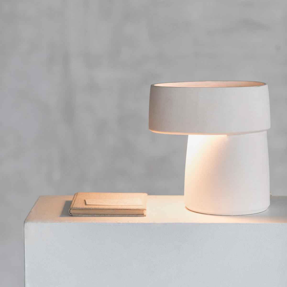 A minimalist white ceramic table lamp casting a soft glow, with wooden coasters nearby.