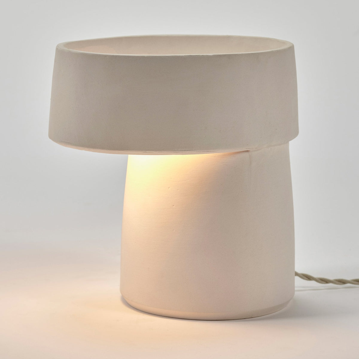 A white ceramic table lamp illuminated, showcasing its warm, ambient light.