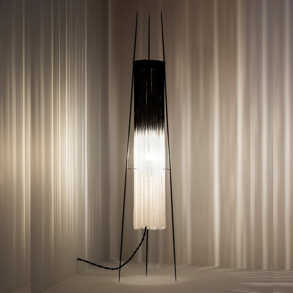 A black and white floor lamp illuminating a textured background.