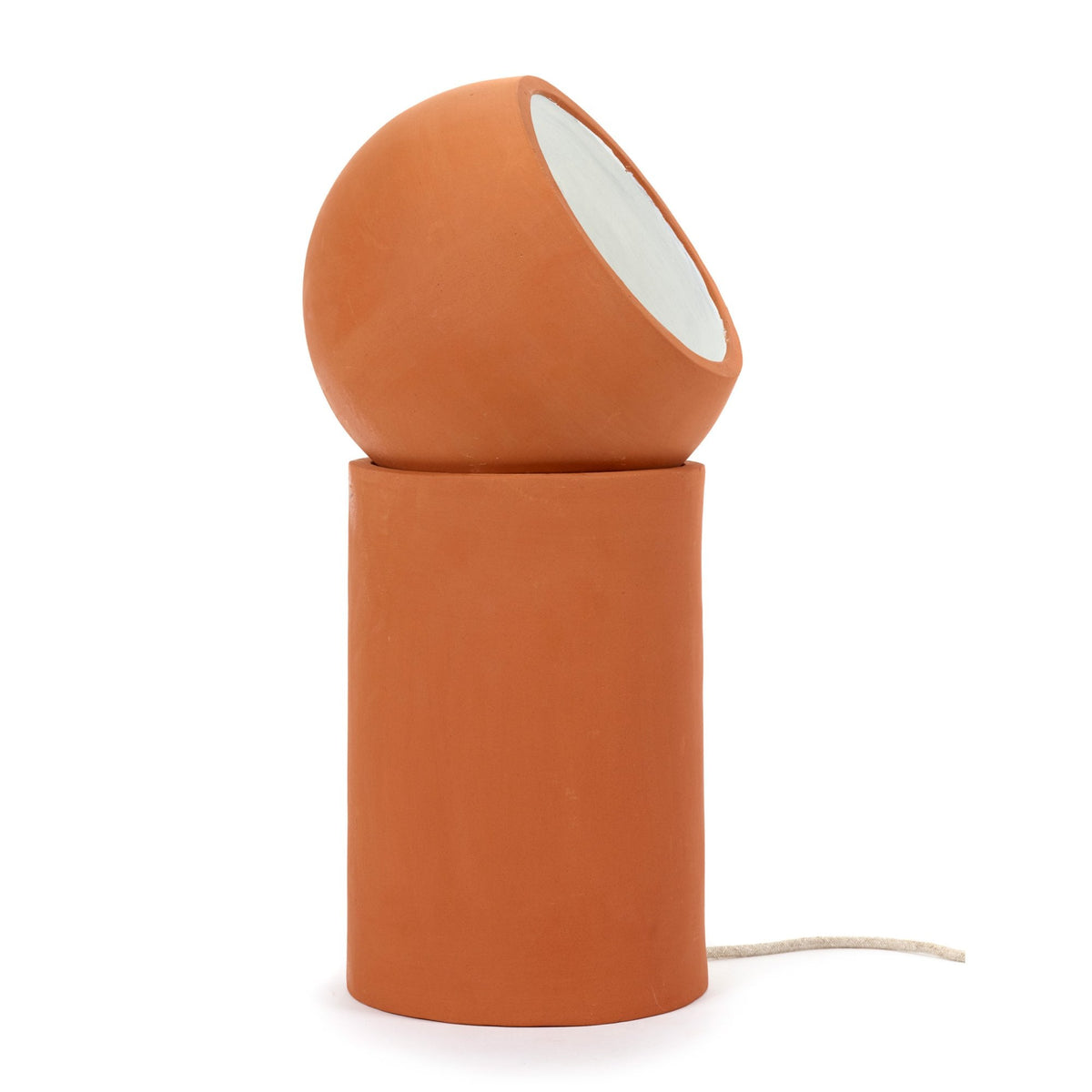 A minimalist terracotta table lamp, cylindrical base with a spherical, angled shade, on a white background.