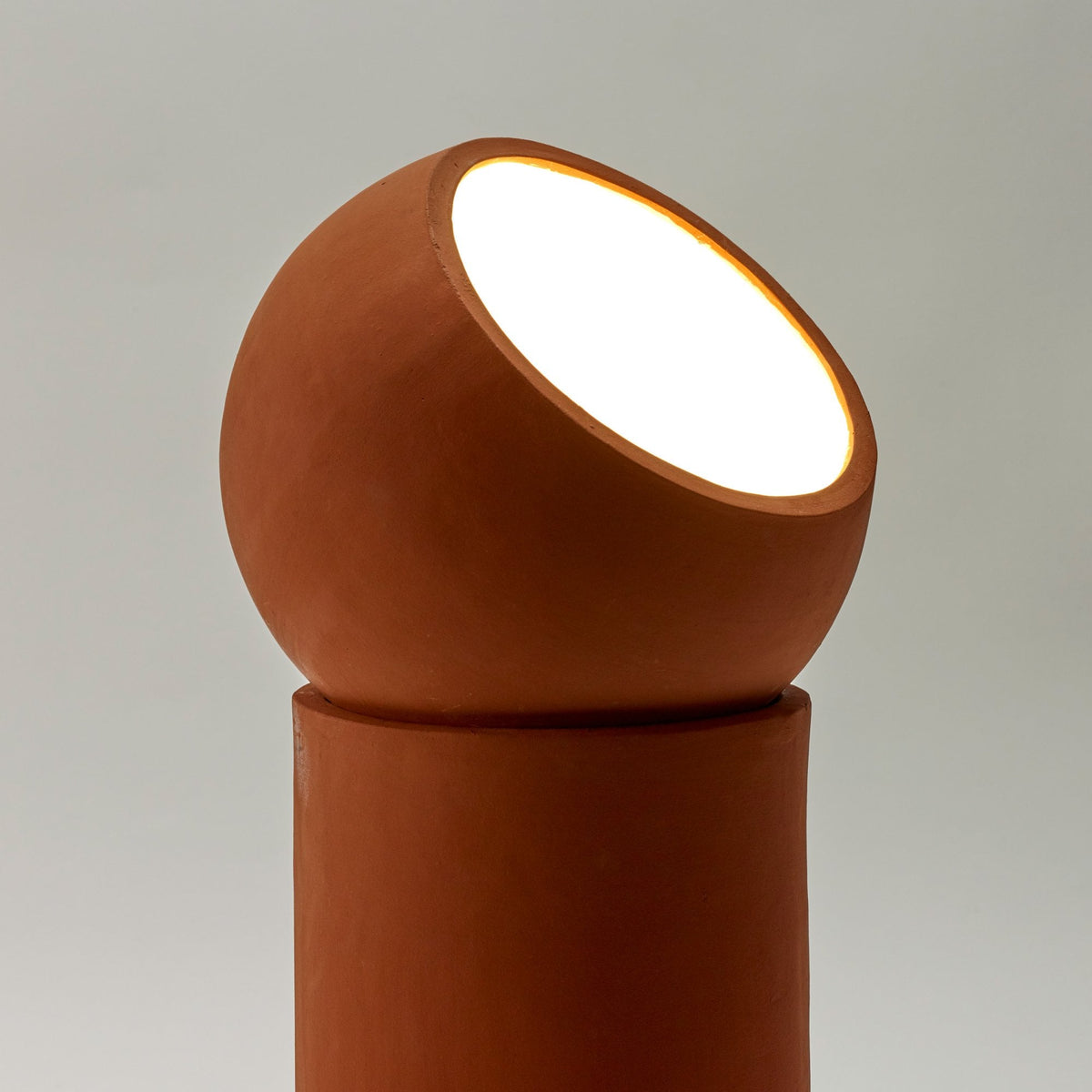 A close-up of a terracotta table lamp with its bright light source illuminating forward.