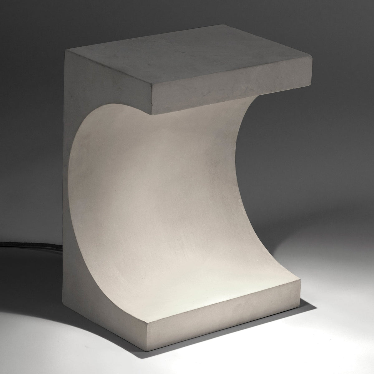 Table lamp made of concrete with a curved cut-out and a warm glow.