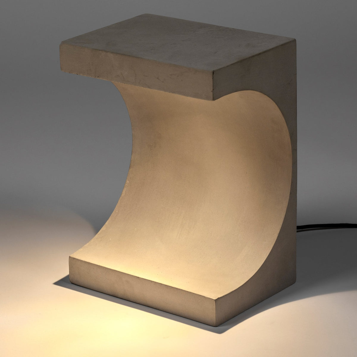 Concrete table lamp with a curved cut-out softly illuminating its surroundings.