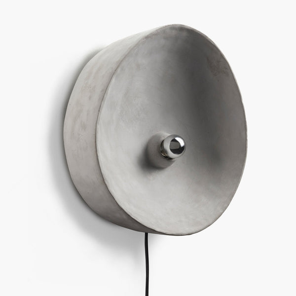 A circular grey wall light with a chrome-capped bulb facing outwards, on a white wall.