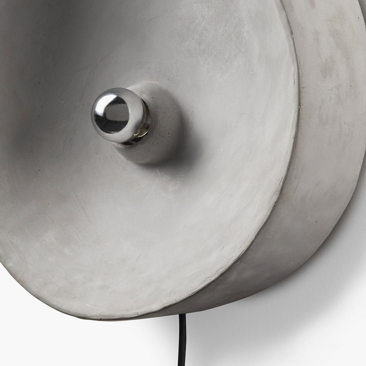 A close-up of a grey circular wall light featuring a small, shiny chrome-capped bulb.