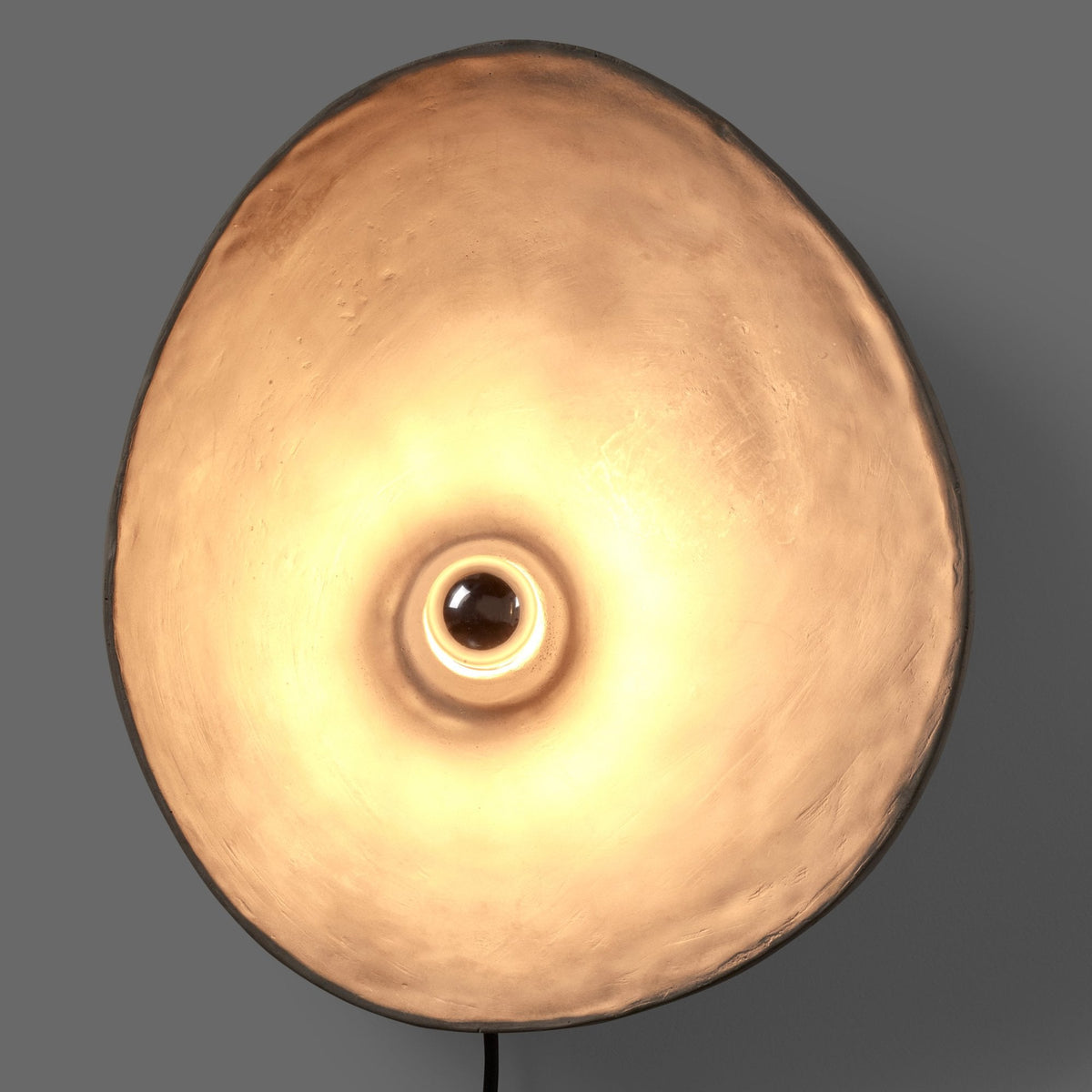 A front view of a grey circular wall light with a warm, glowing bulb providing ambient light.