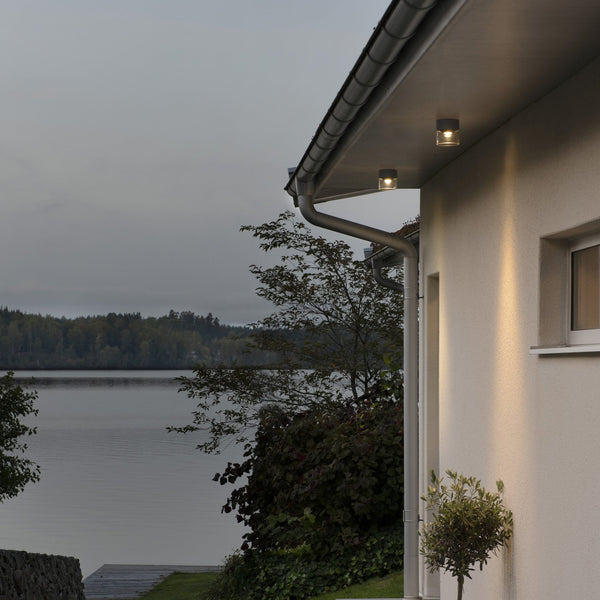 Outdoor ceiling lights fitted under eaves of a house overlooking a lake at dusk.