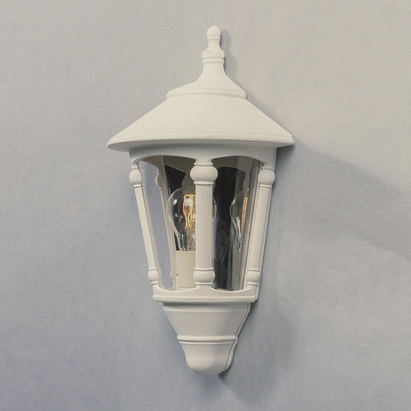 A white outdoor wall lantern with a traditional design, casting a gentle glow on a grey wall.