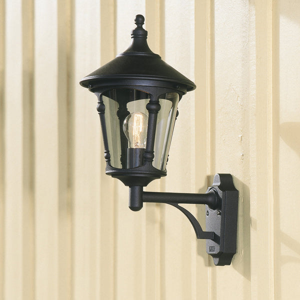 A black outdoor wall light with clear glass panels, fixed to a cream wooden panelled wall.