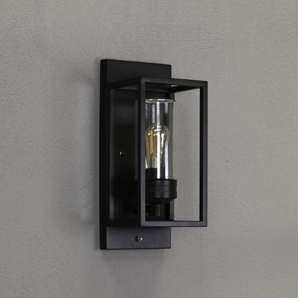 A close-up of a black outdoor wall light with a clear glass shade and exposed bulb.