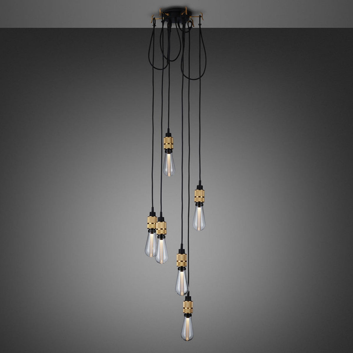 A modern chandelier with six exposed bulbs hanging at varying lengths from a black and gold ceiling mount. 